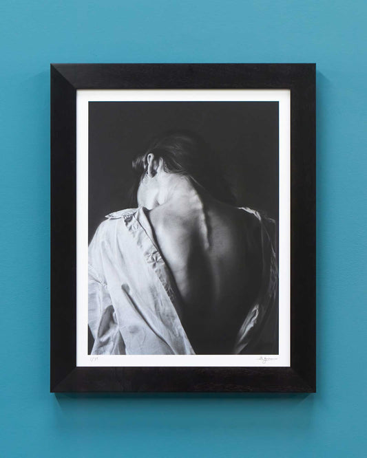 A framed print of a person's bare back and head, mounted in a black frame against a solid blue wall.